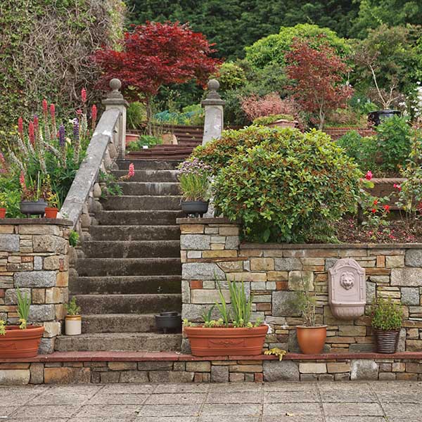Natural stone steps and retaining wall, planter and garden border framing home entrance. Beautiful hardscape, colorful landscape design